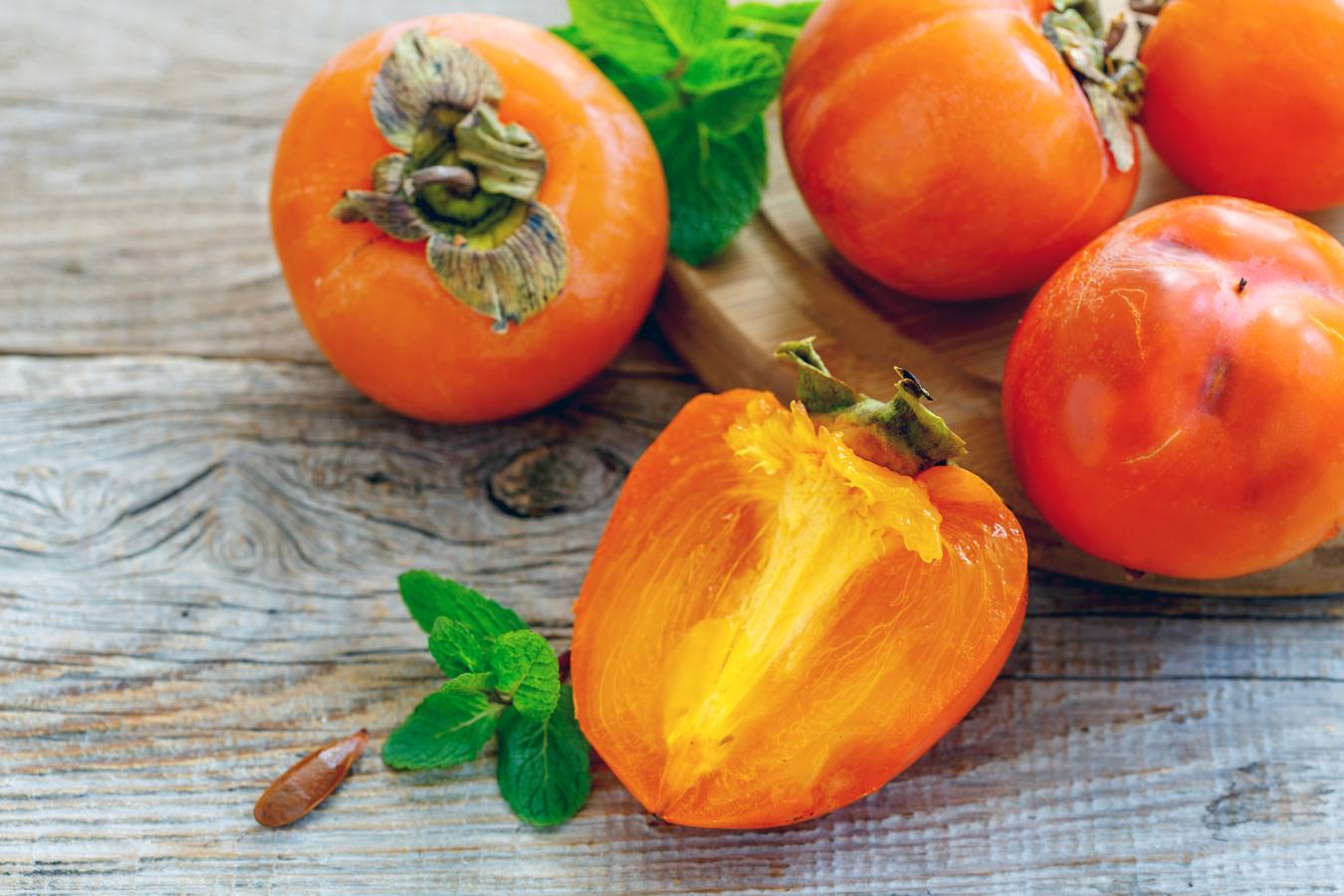 Delicious persimmon fruit and mint on a wooden background.